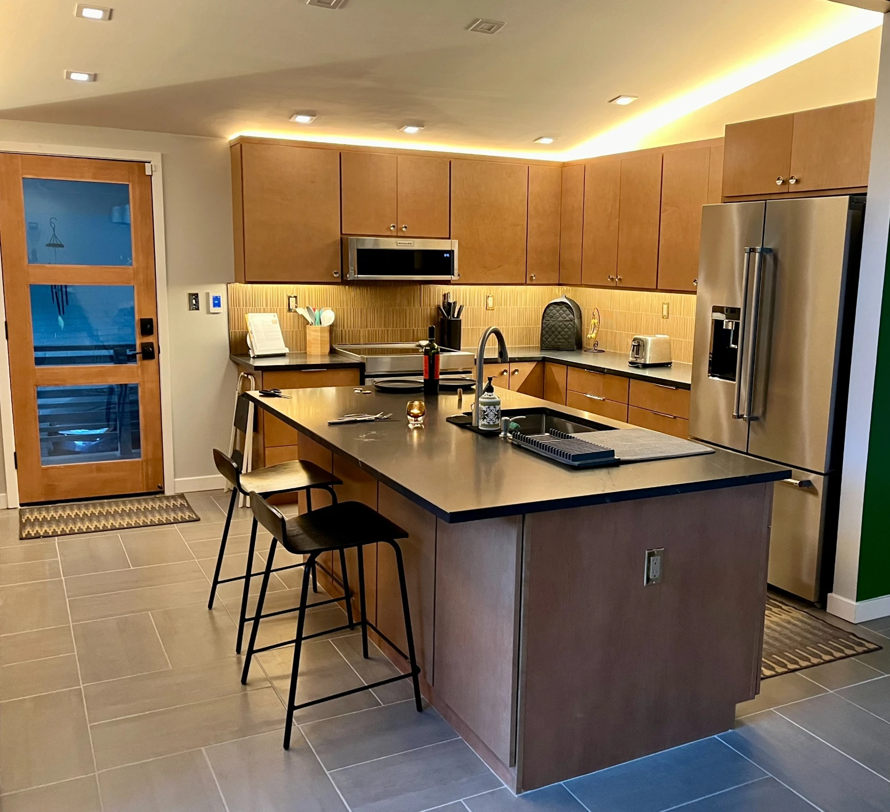 Alexandria kitchen with warm wood cabinetry, a dark island countertop, stainless appliances, and layered lighting
